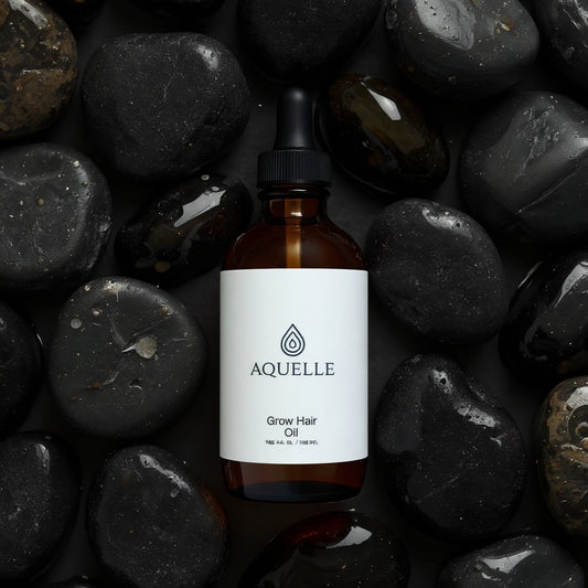 AQUELLE Grow Hair Oil auf nassen schwarzen Steinen – luxuriöses Haaröl für intensives Wachstum und Glanz, präsentiert mit natürlicher Eleganz und Tiefe.
